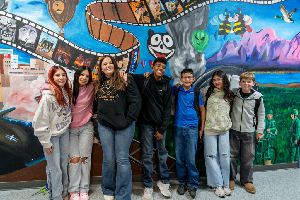 South Valley Prep students smiling in front of a painted school mural