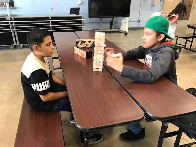 Two students playing Jenga in the cafeteria during the after-school program